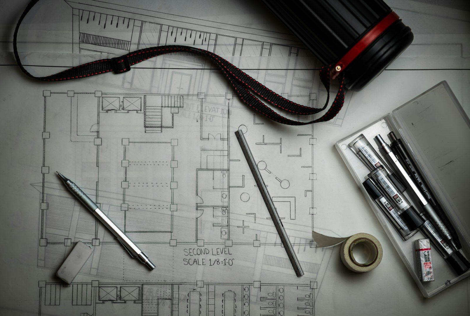 Architectural blueprints of an apartment building spread on a table beside a laptop showing a spreadsheet